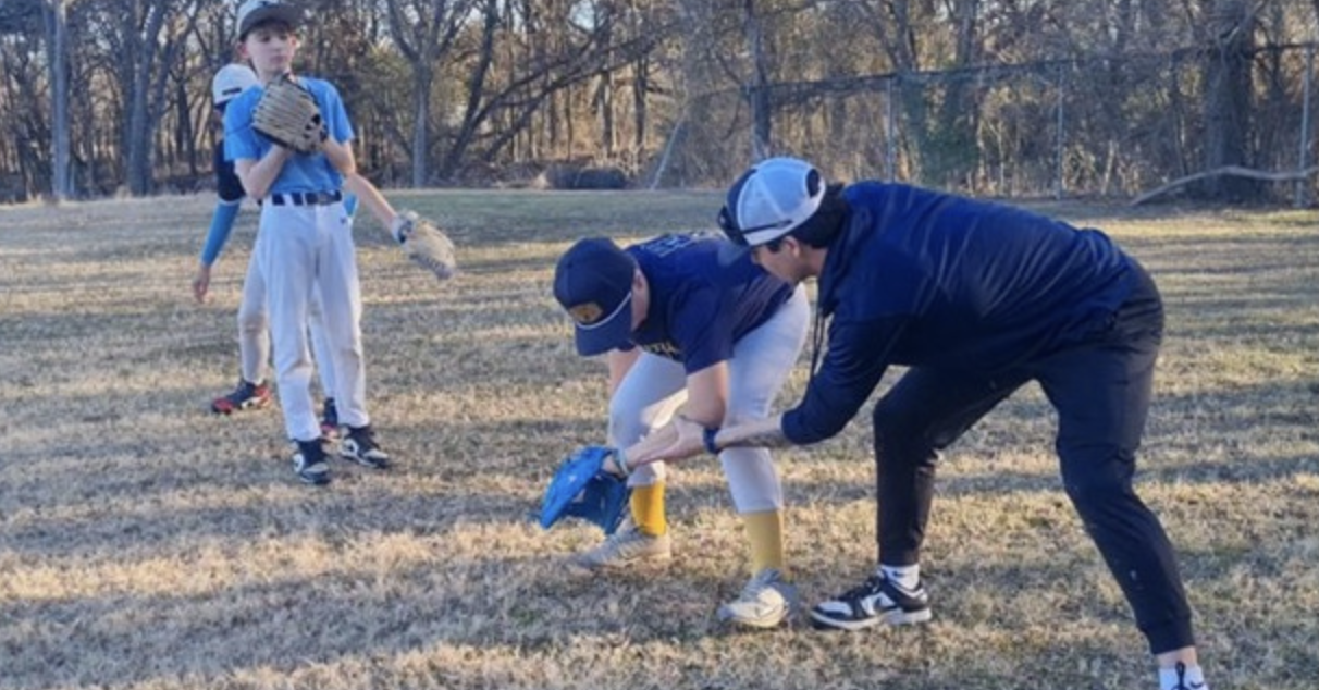Coach teaching boys baseball catching technique outdoors.